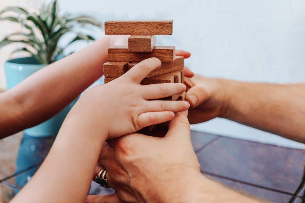 Kinder- und Erwachsenenhände stapeln Holzbausteine zu einem Turm.