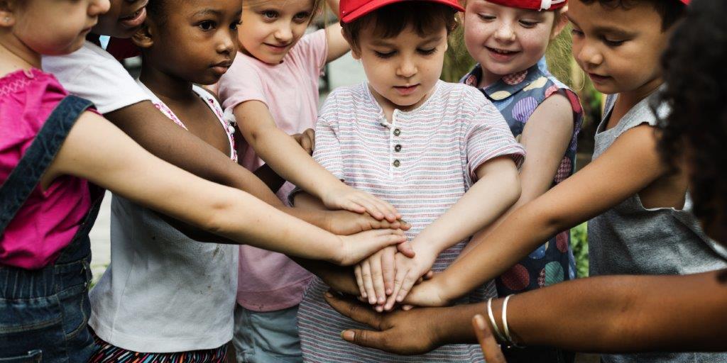 Kinder strecken ihre Hände und stapeln sie in der Bildmitte übereinander.